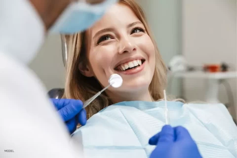 woman smiling during a dental checkup, dentist holding dental tools in gloved hands